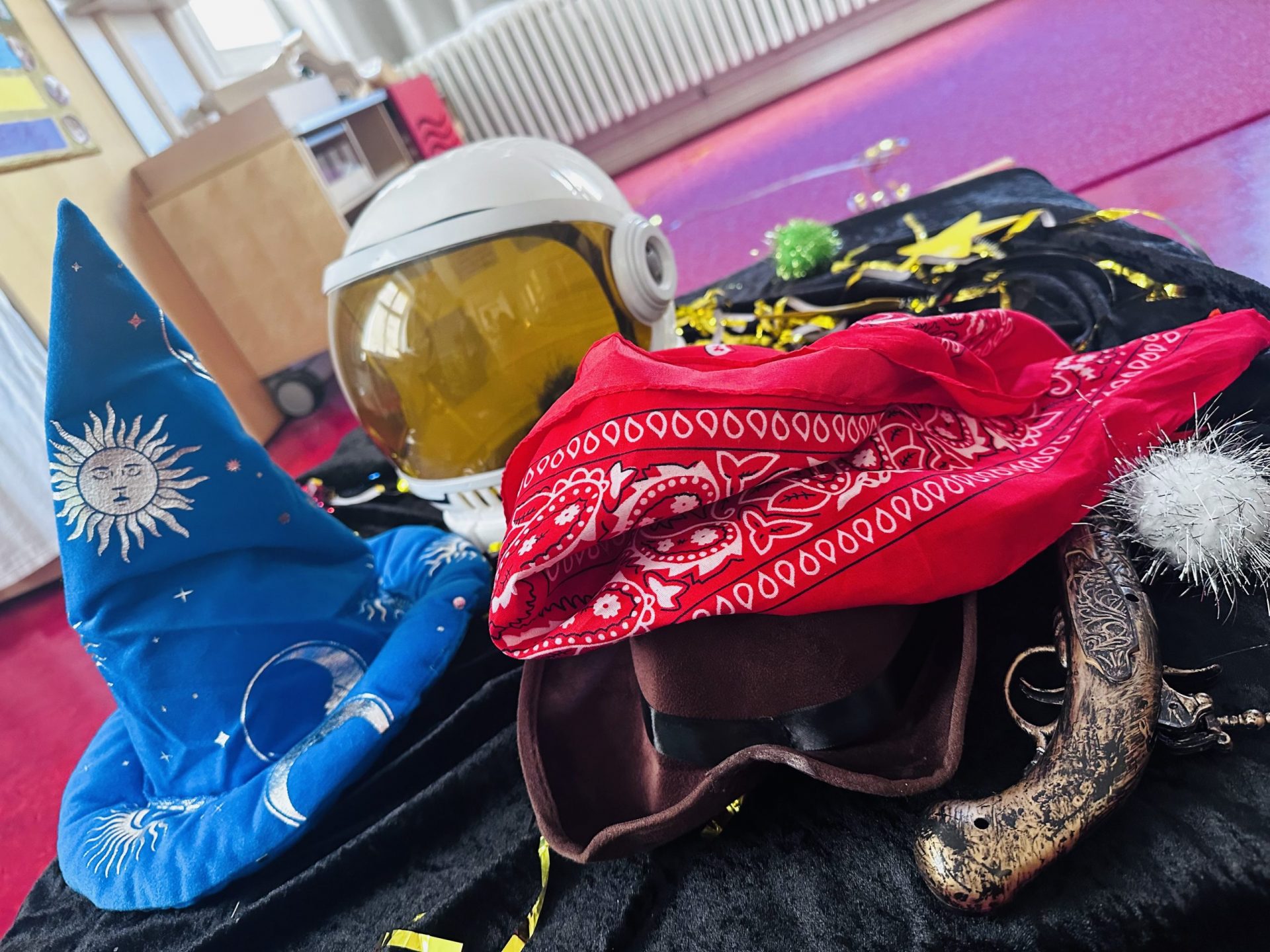 Verkleidungsmaterial in der Kita Puchanstraße in Berlin, darunter ein blauer Zauberhut, ein Astronautenhelm, ein rotes Bandana und eine Spielzeugpistole auf einer schwarzen Decke.